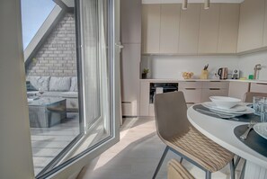 A modern kitchen with a dining area, a view of the outdoors, and a staircase leading to a balcony. - HelApart - Czarna Perła (Hel)