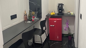 Una cocina compacta con encimera negra, dos taburetes negros, un mini refrigerador rojo, una cafetera y una pequeña orquídea en maceta.