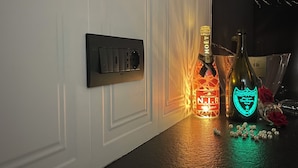 Un enchufe instalado en la pared y dos botellas iluminadas sobre una encimera oscura.