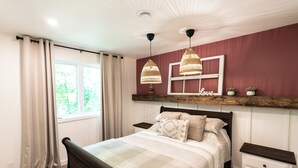 A bedroom with a bed, bedside tables, a window with curtains, and a wall-mounted shelf with a 'Love' sign. - Aux Repères de Papi (Lac-Etchemin)