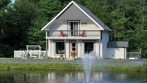 A two-story house with a balcony, a small porch, and a fountain in front. - Aux Souvenirs doux CITQ 303027 (Lac-Etchemin)
