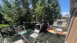 An outdoor patio area with metal chairs and a glass table, surrounded by trees and a view of a mountain.