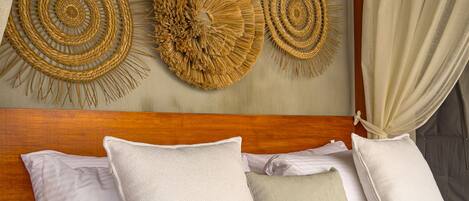 A bed with white bedding, a wooden headboard, and three woven wall decorations.