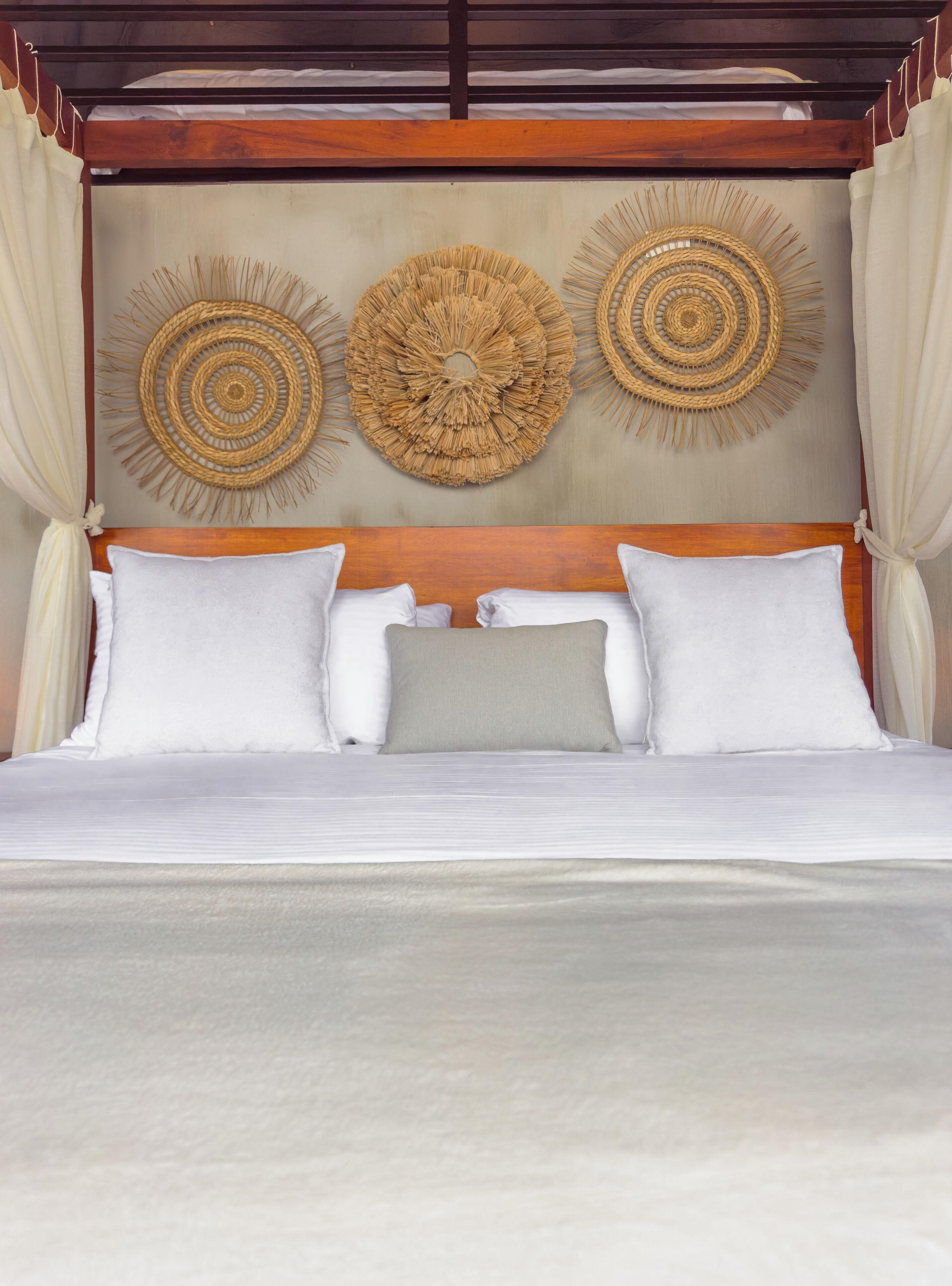 A bed with white and grey pillows, a wooden headboard, and three woven wall decorations.