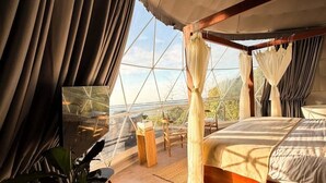 A tented room with a bed, a table with a plant, and a view through the window. - CARDEDEU DOMOS (Santa Tecla)