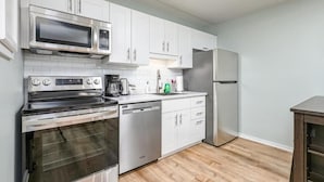 Une cuisine moderne dotée d’appareils électroménagers en acier inoxydable, de meubles de rangement blancs et d’un plancher en bois.