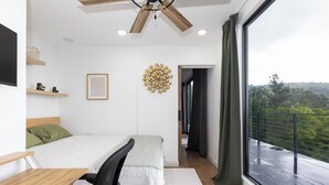 Quarto moderno com cama, escrivaninha, cadeira e vista para uma varanda.
