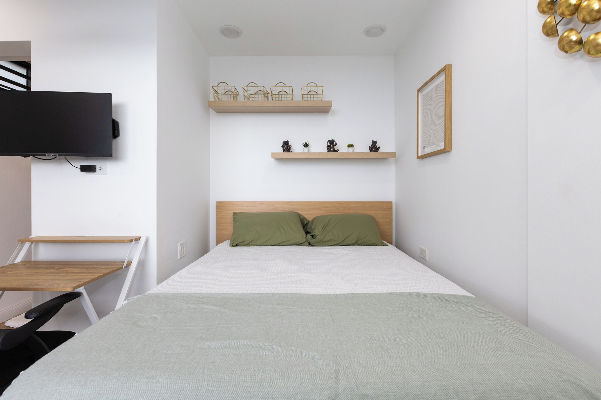 Un dormitorio moderno con una cama, un televisor, un escritorio y estantes con objetos decorativos.