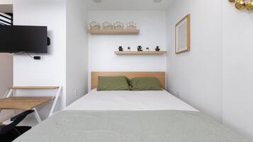 Un dormitorio moderno con una cama, un televisor, un escritorio y estantes con objetos decorativos.