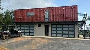Edifício com fachada de metal vermelho, duas portas de garagem e um veículo utilitário preto estacionado na frente.