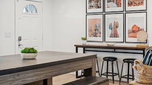 A modern kitchen with a wooden table, bar stools, and framed desert landscape pictures on the wall.
