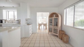 Una cocina moderna con armarios blancos, suelo de baldosas y un comedor con mesa y sillas de madera.