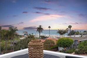 A coastal view from a balcony overlooking a beach with palm trees and a sunset. - Moonlight dream! 4-bedroom, 4-bathroom ocean view home 1 block from the beach. (Encinitas)