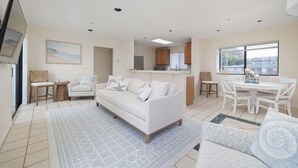 Una sala de estar moderna con un sofá blanco, una mesa de comedor con sillas y una zona de cocina al fondo.