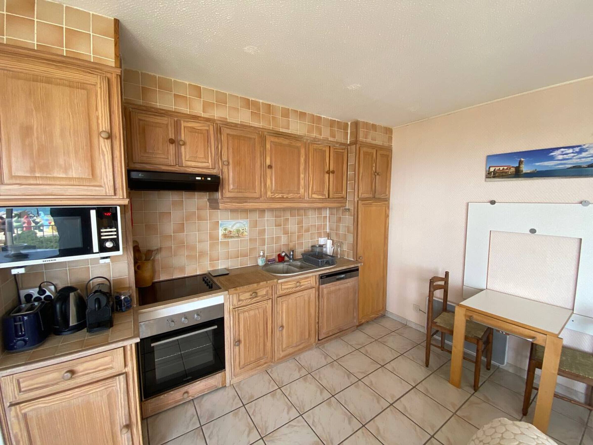 Una cocina compacta con armarios de madera, un microondas, un horno y un pequeño comedor con mesa y sillas.
