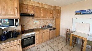 A compact kitchen with wooden cabinets, a microwave, an oven, and a small dining area with a table and chairs. - 2-Room Apartment Sleeps 5 with Parking in Barcarès (Le Barcarès)