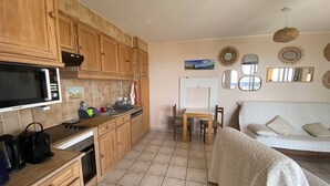 A compact kitchen with wooden cabinets, a microwave, a coffee maker, and a dining area with a table and chairs. - 2-Room Apartment Sleeps 5 with Parking in Barcarès (Le Barcarès)