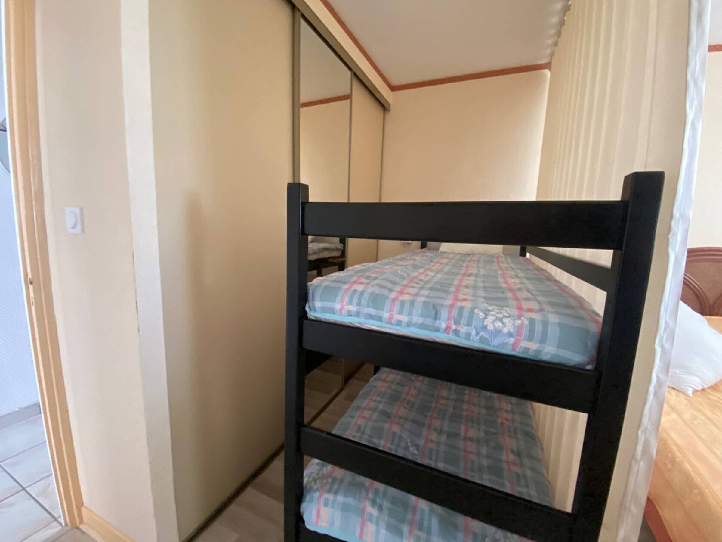 Een stapelbed met een geruit matras in een kamer met kale muren en een zichtbare deur.