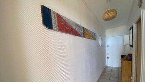 A hallway with a textured wall, a hanging woven light fixture, and a wooden cabinet with items on top. - 2-Room Apartment Sleeps 5 with Parking in Barcarès (Le Barcarès)