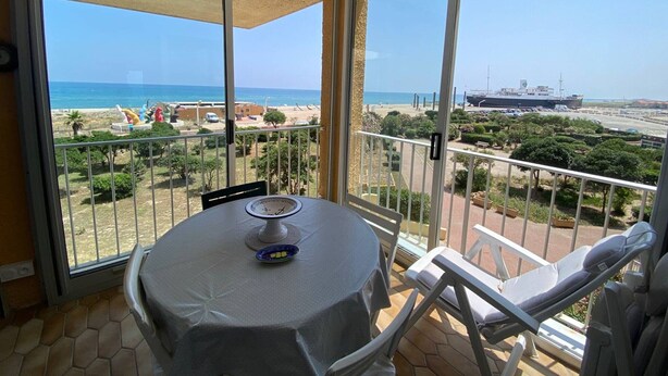 A balcony with a table and chairs, overlooking a beach and a ship. - 2-Room Apartment Sleeps 5 with Parking in Barcarès (Le Barcarès)