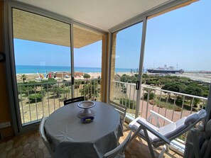 Ein Balkon mit Tisch und Stühlen, mit Blick auf einen Strand und ein Schiff.