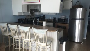 A kitchen with a wooden island, white bar stools, stainless steel appliances, and a trash bin.