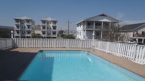 A rectangular swimming pool with a wooden deck and a white fence.