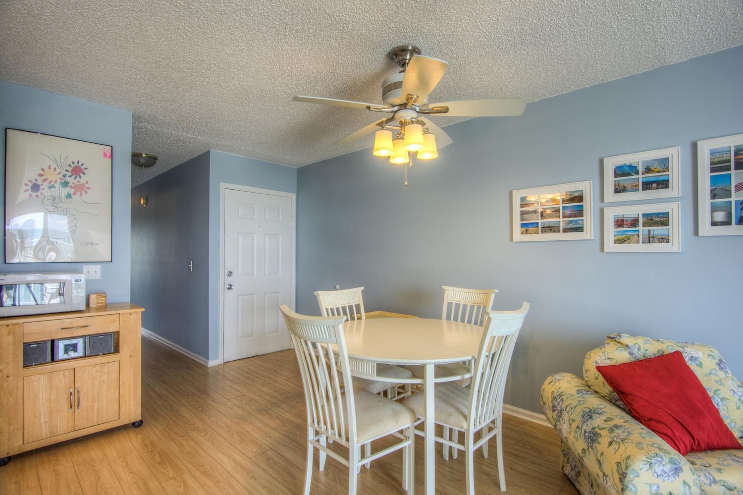 A dining area with a white table and chairs, a ceiling fan, and framed pictures on the wall.