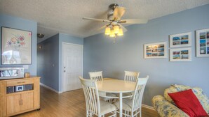 A dining area with a white table and chairs, a ceiling fan, and framed pictures on the wall.