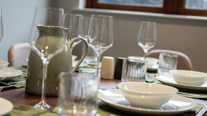 Una mesa de comedor dispuesta con cristalería transparente, platos blancos y una jarrón.