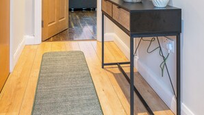 Un pasillo con una puerta de madera, una consola con una lámpara y un espejo.