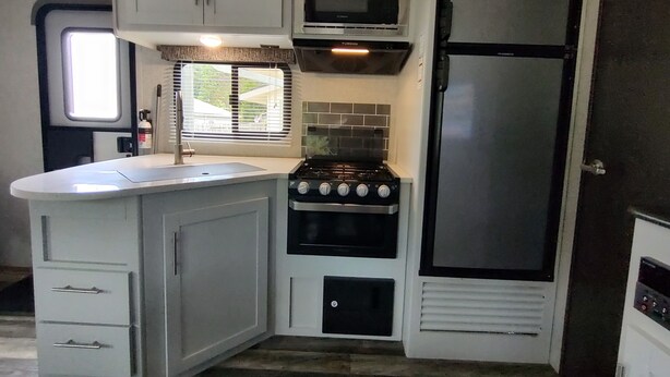 A compact kitchen with a sink, stove, microwave, and refrigerator. - Cozy RV in Quaint Klamath with AC, WiFi, DISH network, fully hooked up. (Klamath)