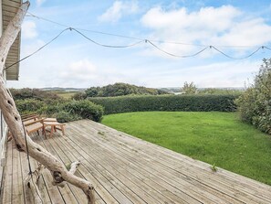 Eine Holzterrasse mit Gartenmöbeln, einem gepflegten Rasen und einer Hecke.