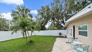 A backyard with a white fence, a palm tree, and a patio with two chairs and a table. - The Seapearl at UTC-1/1 Guest Suite (Sarasota)