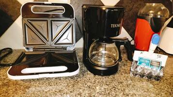 A kitchen with a sandwich maker, a coffee maker, and a box of coffee pods.