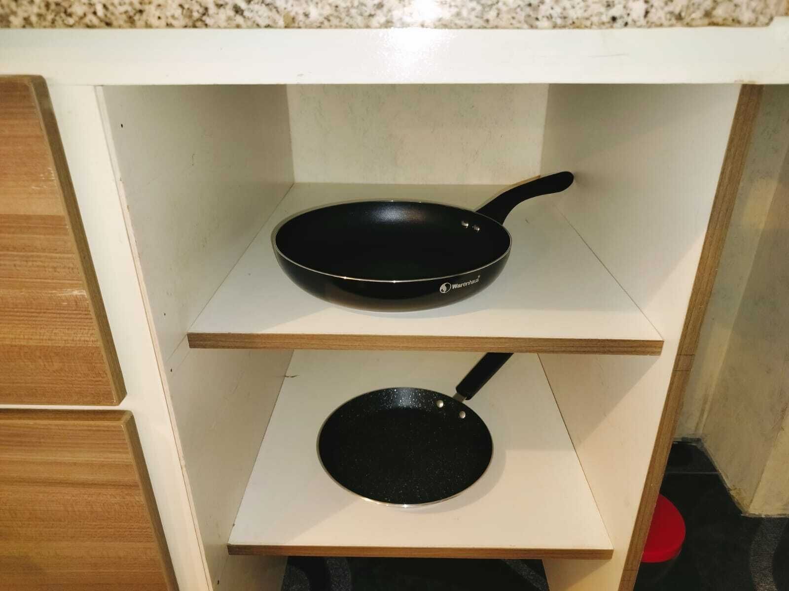 A kitchen with two black pans on white shelves.