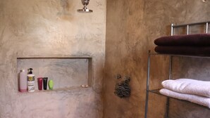 A bathroom with a shelf holding toiletries, a towel rack with towels, and a shower area.