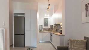 Een kleine keuken met een inbouwkoelkast, een eethoek met een tafel en stoelen, en een woonkamer met een bank en een plant.