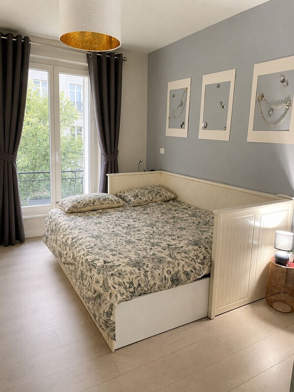 Un dormitorio con cama, cortinas, una ventana y adornos en la pared.