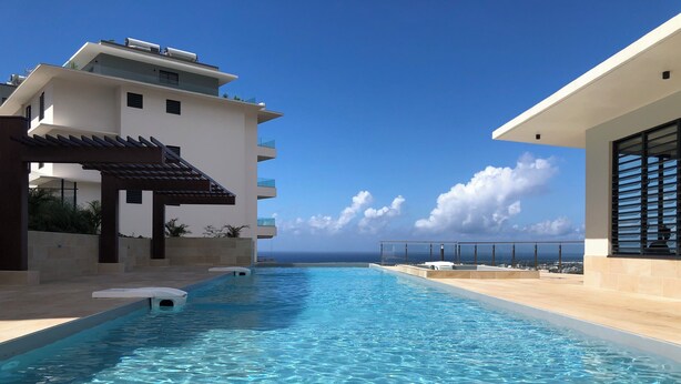 Ein moderner Poolbereich mit klarem, blauen Wasser, Blick auf den Ozean und ein Gebäude mit Balkonen.