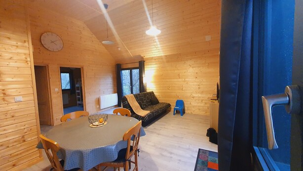 A cozy wooden cabin interior with a dining table, chairs, a sofa, and a clock on the wall. - Chalet with terrace and garden 5 minutes from the village, near lake and ski resorts (La Tour-d'Auvergne)