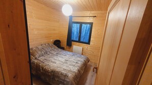 A small, wooden cabin bedroom with a bed, a window, and a radiator. - Chalet with terrace and garden 5 minutes from the village, near lake and ski resorts (La Tour-d'Auvergne)