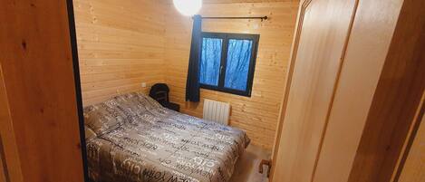 Pequeño dormitorio de cabaña de madera con cama, ventana y radiador.