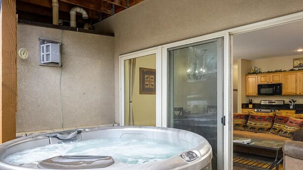 Un bain à remous situé dans un espace extérieur abrité, avec une porte-fenêtre coulissante donnant sur la cuisine et le salon.