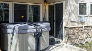 Un bain à remous situé à l’extérieur d’une maison, avec un mur en pierre, une porte et une fenêtre.
