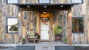 A wooden house with a white front door, a number plaque '1035', and a bench with potted plants in front.