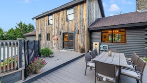 A rustic log cabin with a deck, outdoor seating, and a stone chimney.