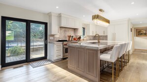 A modern kitchen with a large island, white cabinetry, and a view to the outdoors.