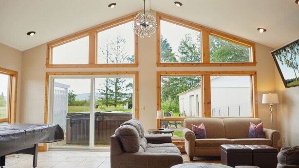 Un salón amplio con techo alto, ventanas grandes, mesa de billar y una zona de estar acogedora.