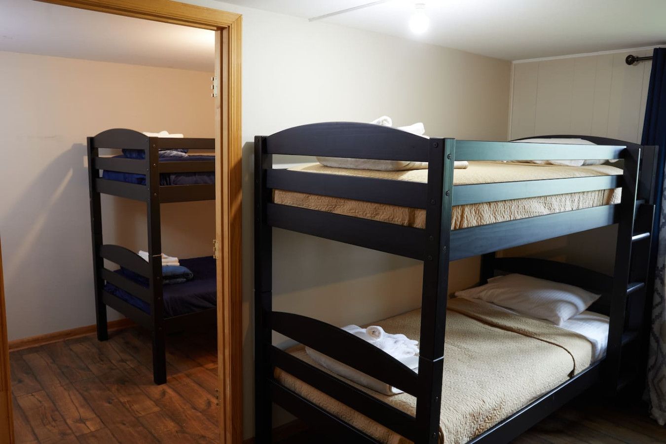 Een kamer met twee stapelbedden, houten vloeren en een deur naar een andere kamer.
